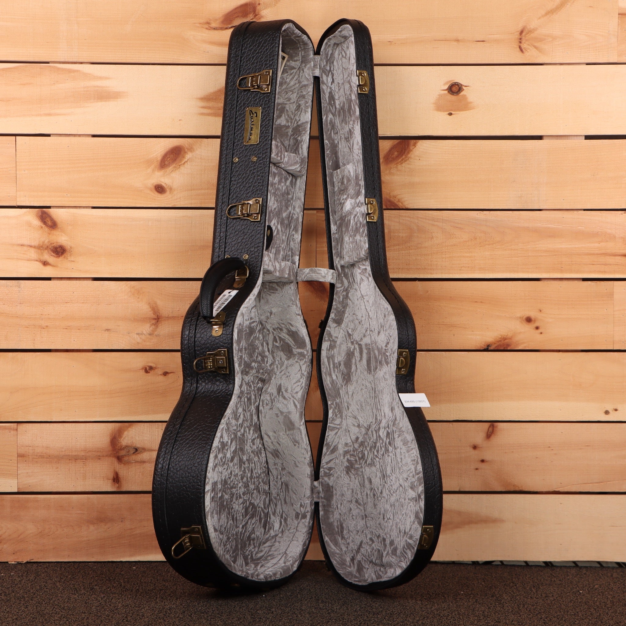 Eastman E20OMMRTC natural acoustic guitar case open showing gray velvet interior with brass hardware