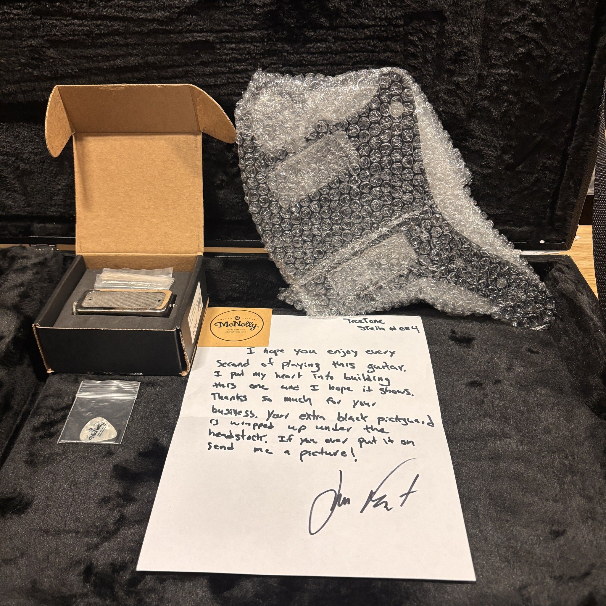 Treetone Stella Vintage White guitar accessories package with McNelly pickup, guitar pick, and handwritten builder's note