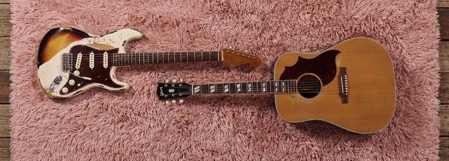 Two guitars on a pink rug with a wooden floor background